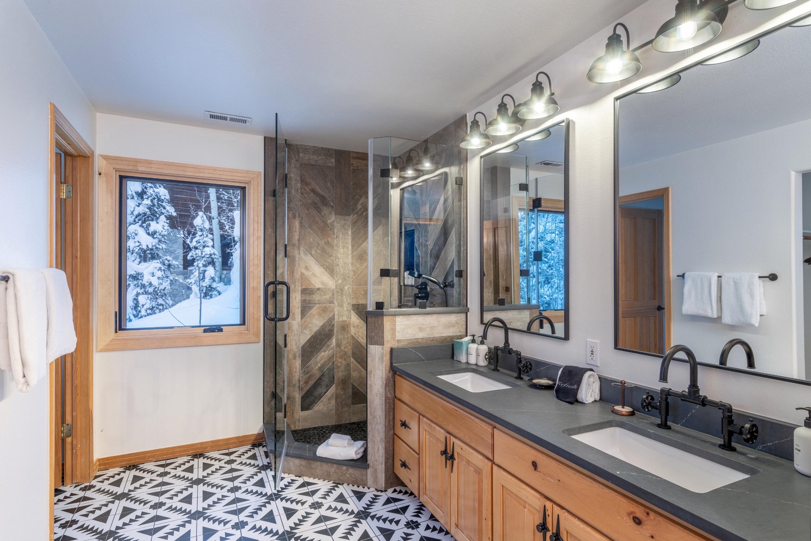 Luxurious master bathroom with dual vanities, spacious glass shower, and stunning winter mountain views through large windows for your ultimate relaxation.