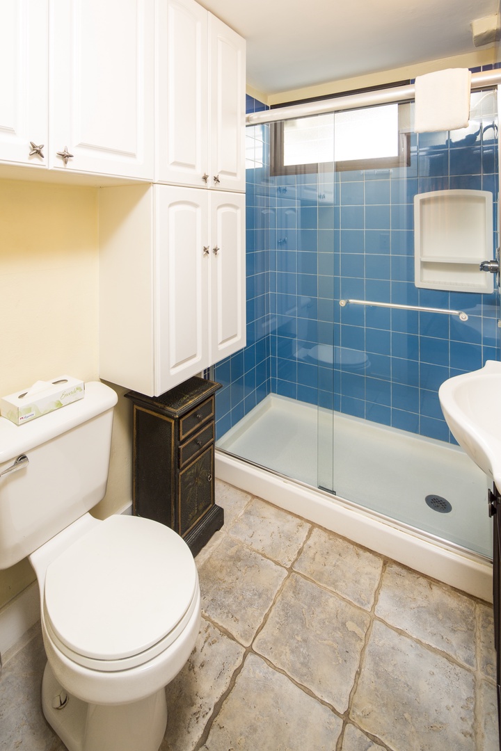 Bright and spotless bathroom featuring a refreshing walk-in shower, ample cabinet storage, and a window to let in natural light during your stay.