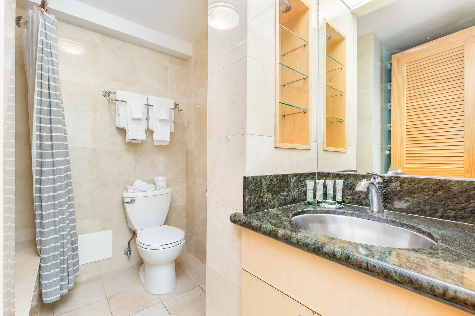 Your private bathroom features a granite vanity, glass shelving, and fresh towels, with a tub-shower combo ready for your arrival.