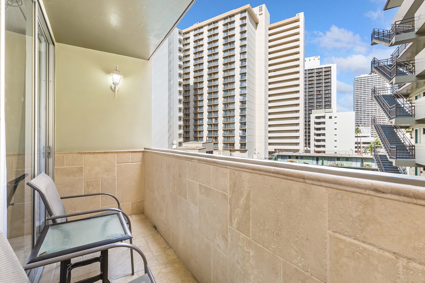 Private balcony overlooking an urban cityscape with high-rise towers. Tiled walls and a comfortable chair create a spot to enjoy the open air.