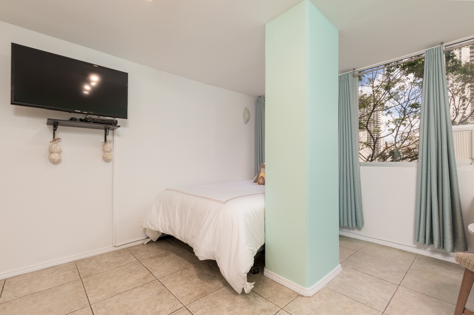 Your restful bedroom features a plush bed, wall-mounted TV for entertainment, and bright windows framing serene outdoor views—perfect for unwinding after exploring.