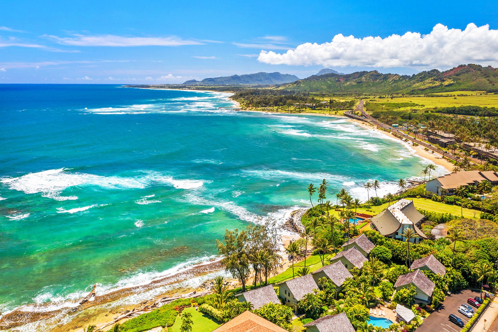 Stunning aerial view showcases pristine beachfront properties nestled between turquoise waters and lush tropical mountains.