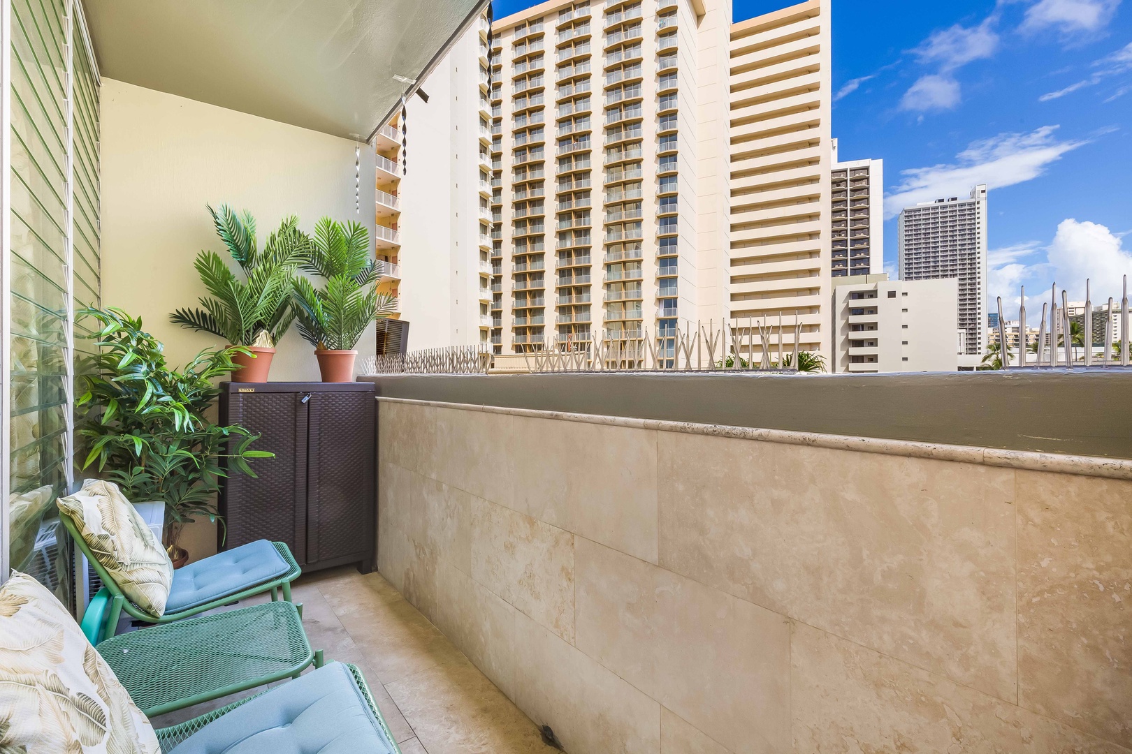 Step onto your private balcony and breathe in the fresh island air. Lush potted palms frame your urban retreat, where comfortable seating invites you to relax and soak in vibrant Honolulu views—a peaceful oasis above the city.