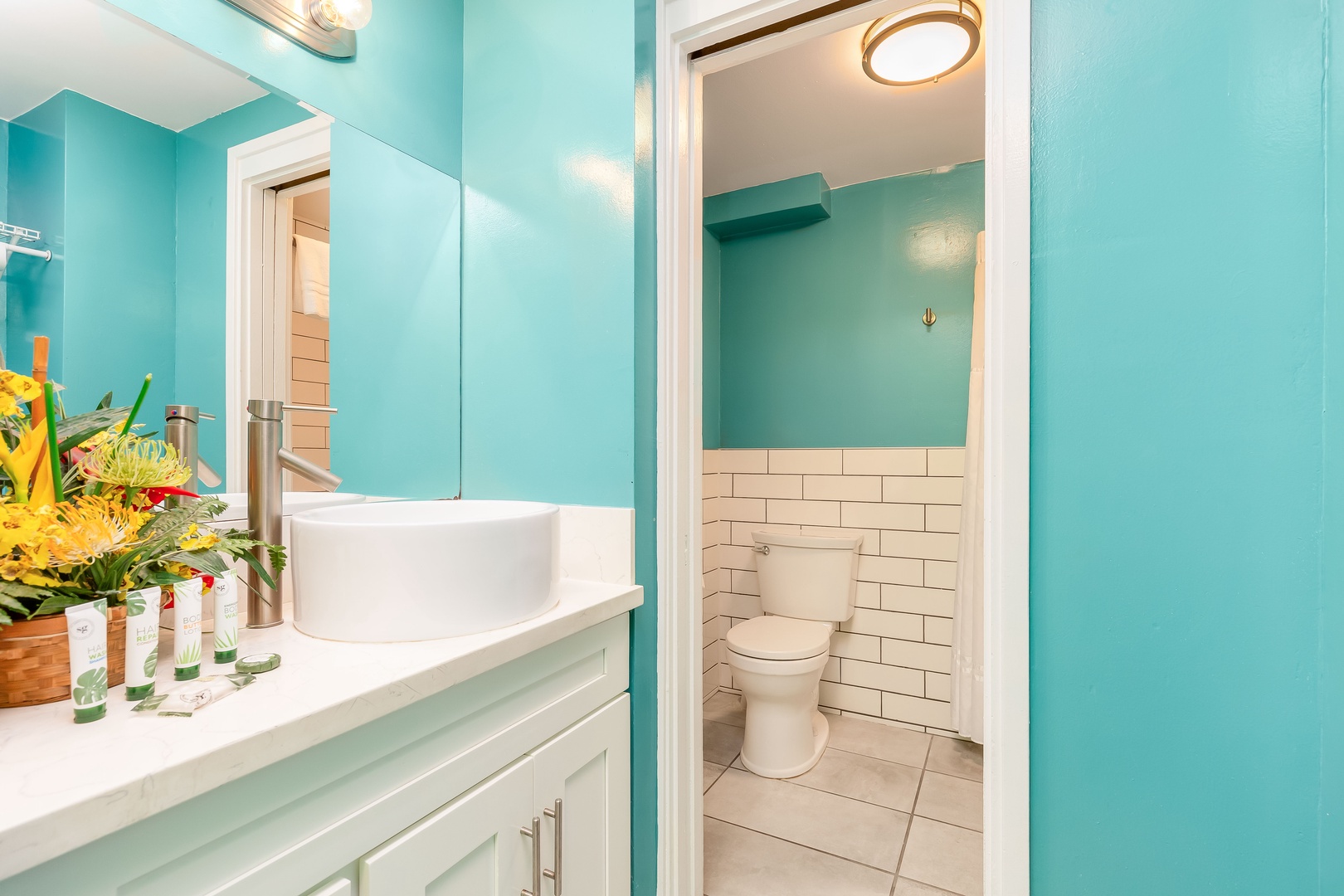 Step into your bright, beachy bathroom where turquoise walls evoke coastal tranquility. Fresh flowers welcome you at the vanity, and crisp white subway tile adds timeless charm to your private retreat.