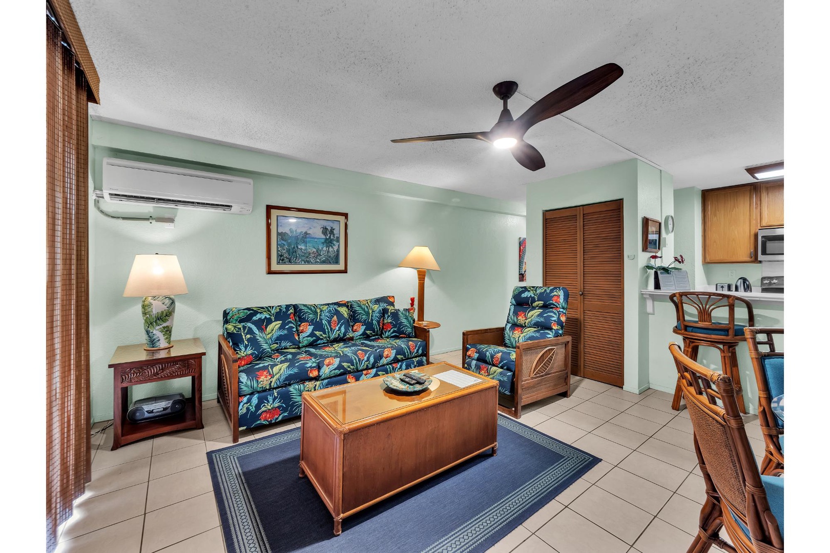 Relax in your tropical-themed living space with comfortable seating, ceiling fan, and convenient kitchenette for easy vacation living.