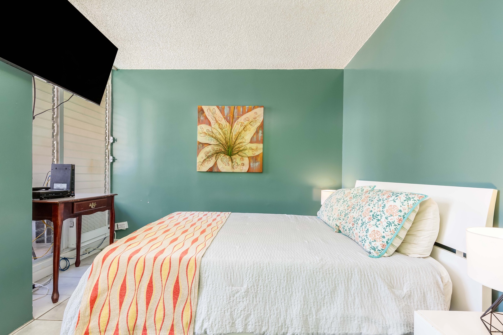 Sink into the plush bed surrounded by soothing turquoise walls, tropical artwork, and bright natural light streaming through your private outdoor access.