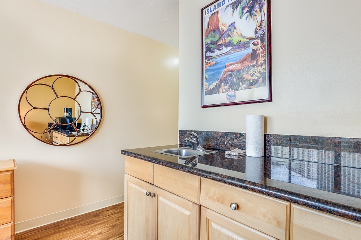 A cozy kitchenette awaits with gleaming granite countertops, a stainless steel sink, and warm wood cabinetry. The island-inspired artwork adds a tropical touch to your private retreat.