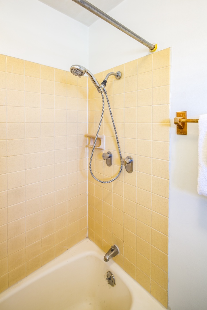 Bright, tiled tub-and-shower combo ready for your refreshing morning routine or relaxing evening soak. Soft towels hang nearby for your comfort.