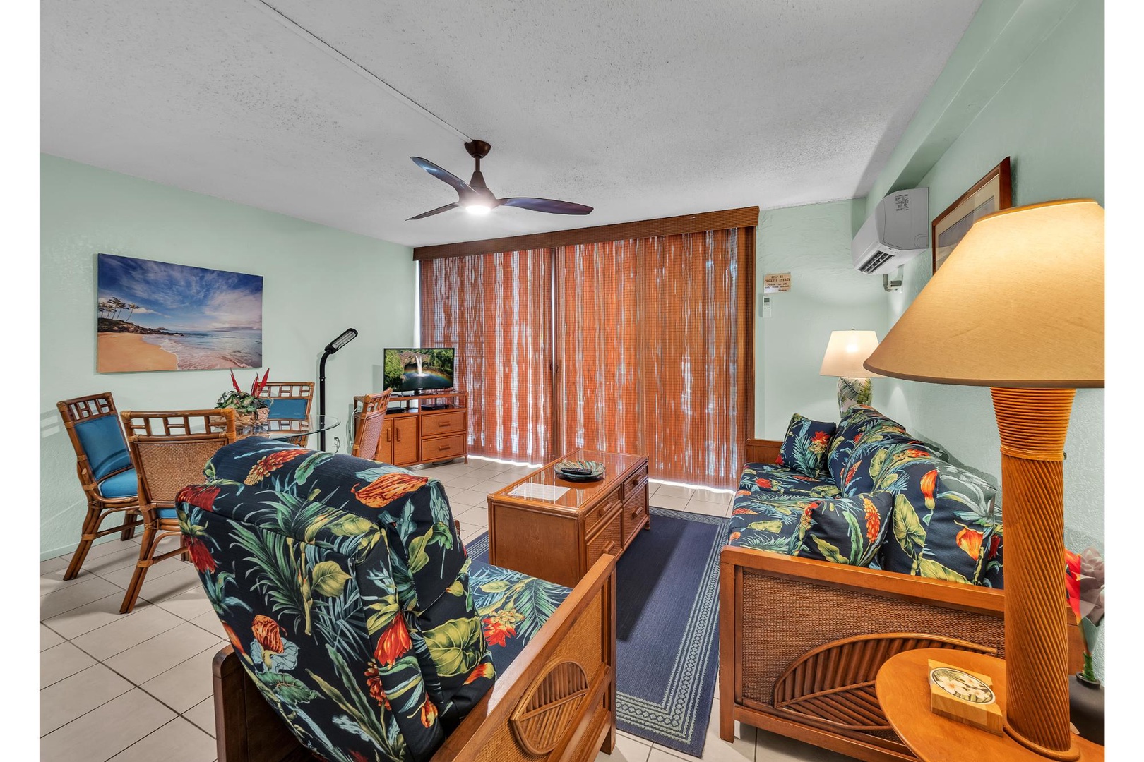 Sink into tropical comfort in your bright living space with vibrant Hawaiian-print furnishings, cooling ceiling fan, and beachside artwork.