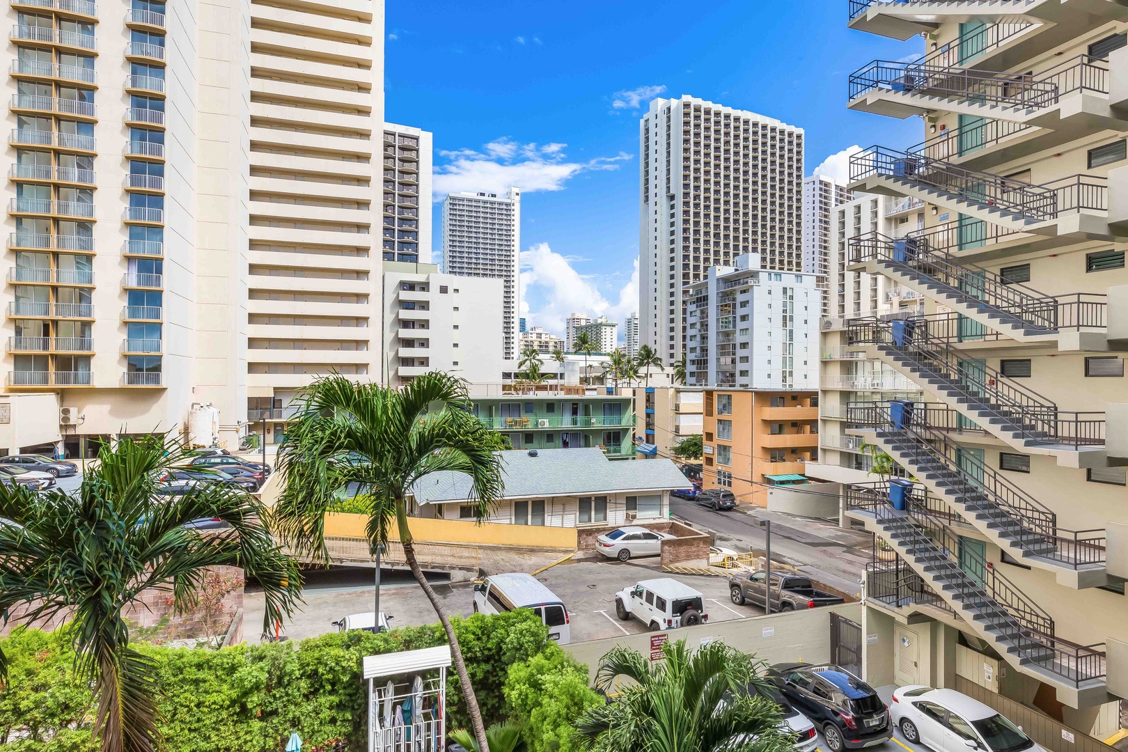 The property is situated in a vibrant urban district, surrounded by high-rise buildings and accessible parking, with tropical palm trees dotting the neighborhood landscape.