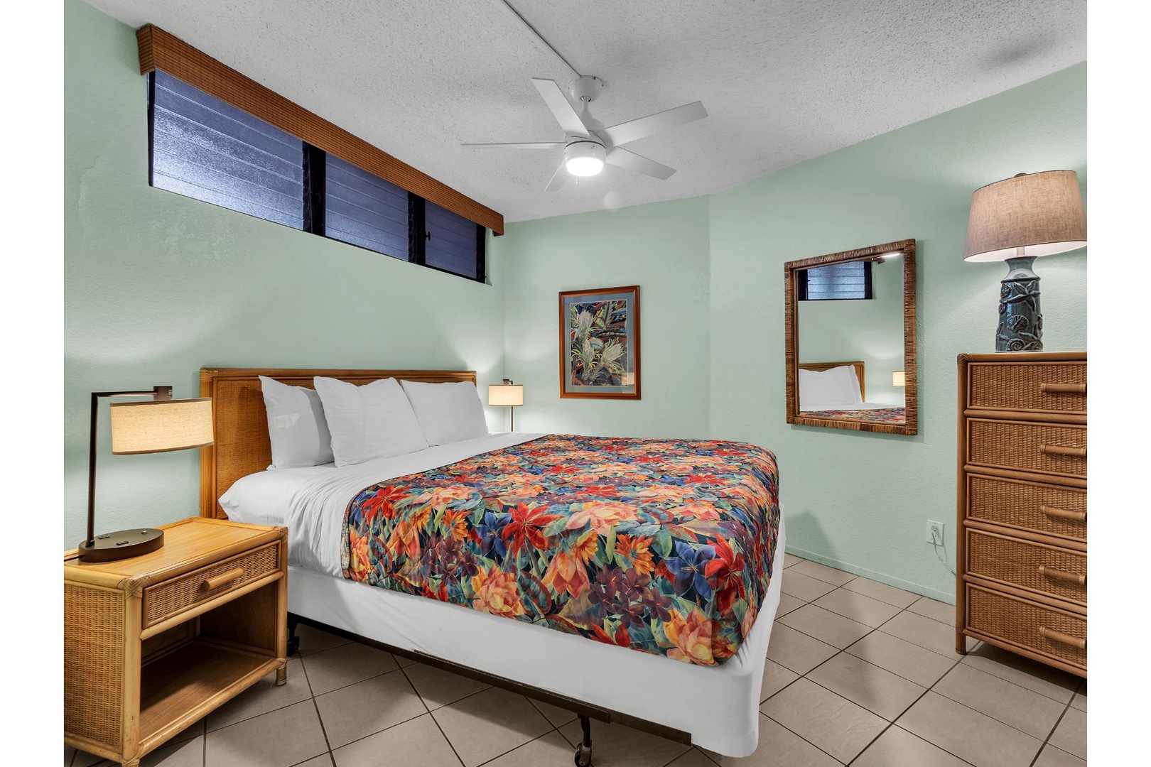 Unwind in your tropical-themed bedroom featuring warm bamboo furnishings, ceiling fan, and vibrant floral bedding that brings island vibes to your stay.