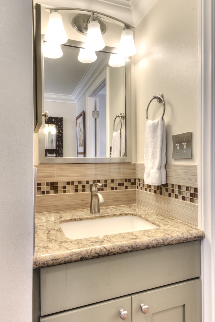 Step into your beautifully updated bathroom featuring a granite vanity with mosaic tile backsplash, polished fixtures, and soft lighting that creates the perfect space to refresh and unwind.