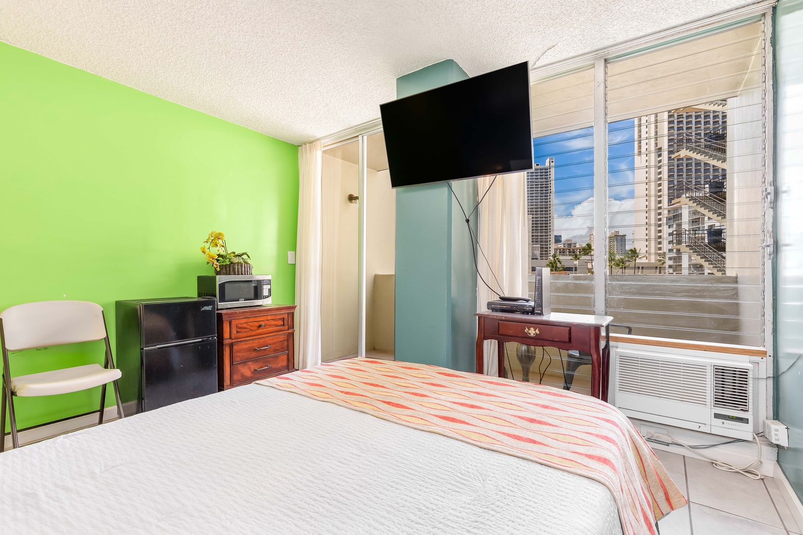 Your bright bedroom features a comfy bed, flat-screen TV, mini-fridge, and microwave—plus a window air conditioner to keep you cool while you enjoy city views.