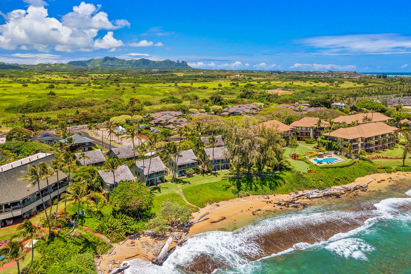 Stunning beachfront resort with mountain backdrop and pristine sandy shore surrounded by tropical landscaping.