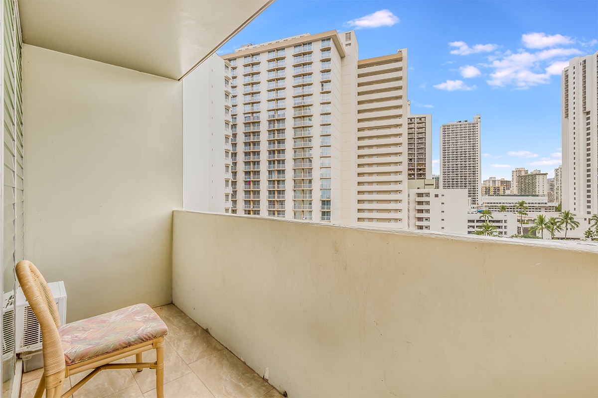 A private urban balcony overlooks high-rise buildings and palm trees scattered throughout the vibrant cityscape under a clear blue sky.