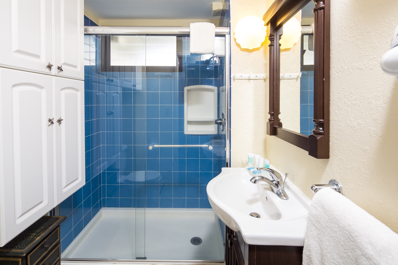 Refresh in your private bathroom with its sleek glass-enclosed shower and vibrant blue tiles. Fluffy towels await, and warm lighting creates a welcoming retreat after a day of exploring.