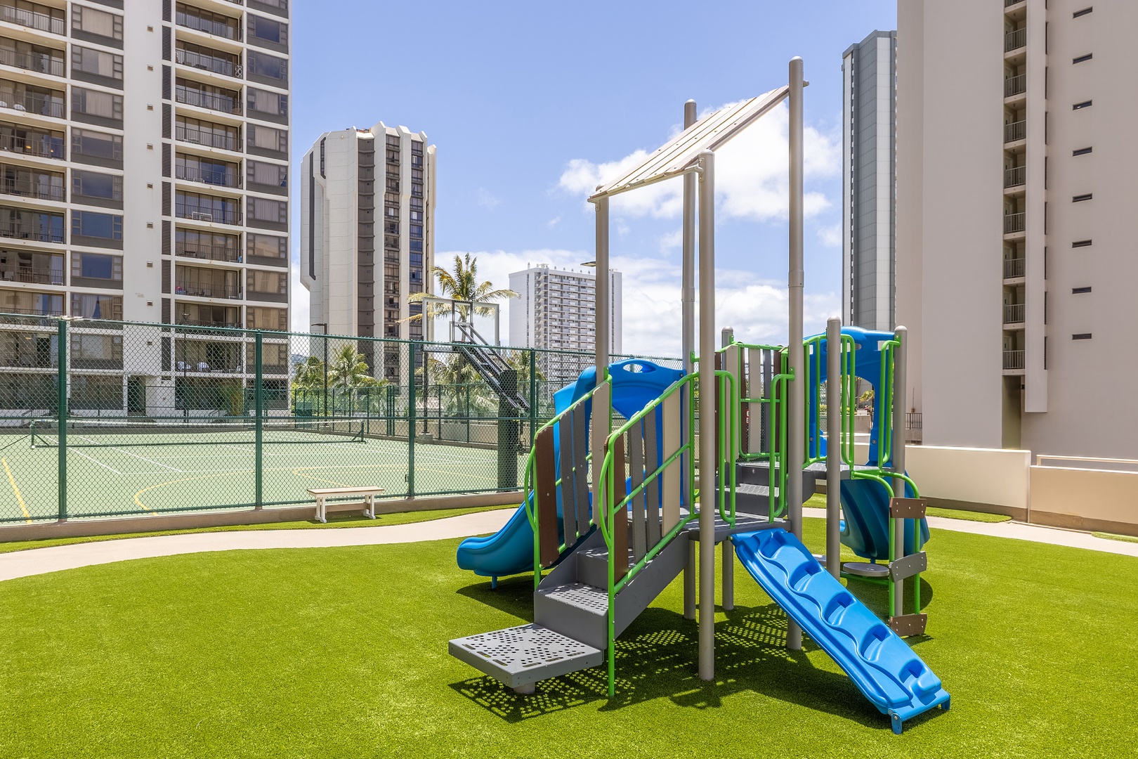 A vibrant playground with slides and climbing structures sits on soft turf, perfect for little ones to play while you relax nearby under sunny Hawaiian skies.