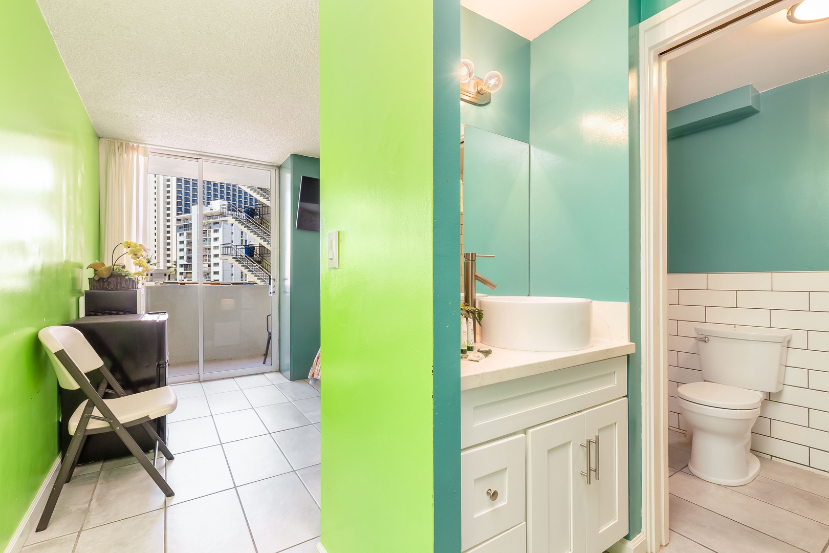 Modern bathroom with crisp white subway tile and a sleek vanity leads to a bright balcony with city views you can enjoy during your stay.