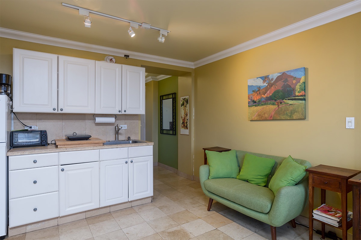 Settle into your cozy living space where cheerful yellow walls and a plush green sofa create a warm, inviting atmosphere. Your fully equipped kitchenette makes light cooking a breeze.