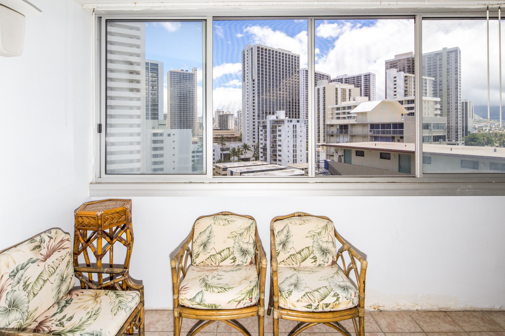 A bright urban skyline stretches beyond the windows of your private retreat, where tropical-inspired seating invites you to unwind with sweeping city views.