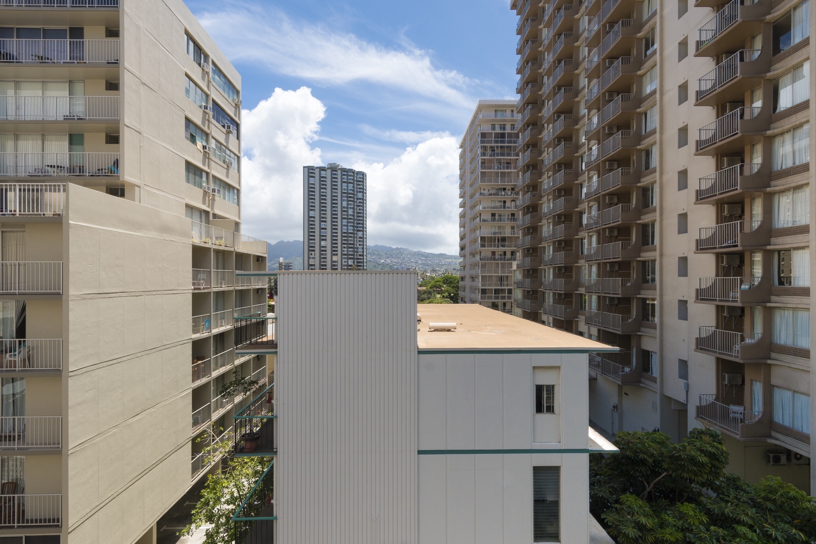 Urban setting with mid-rise and high-rise buildings framing mountain views in the distance, captured from street level on a partly cloudy day.