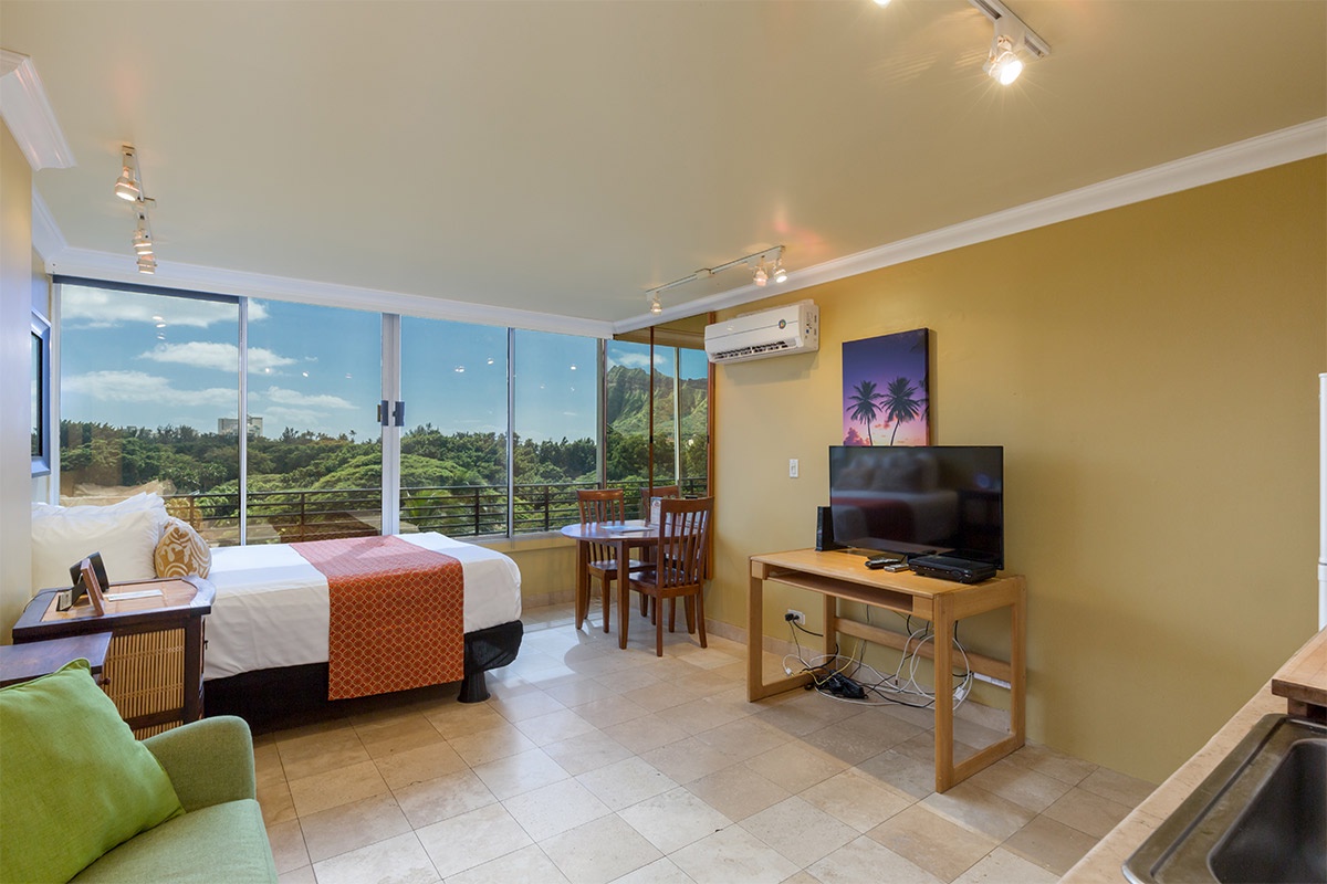 Picture yourself waking up to this stunning natural vista. Sunlight streams through expansive windows, revealing lush greenery beyond. Your cozy retreat includes air conditioning, a flat-screen TV, and dining table—everything you need for a perfect escape