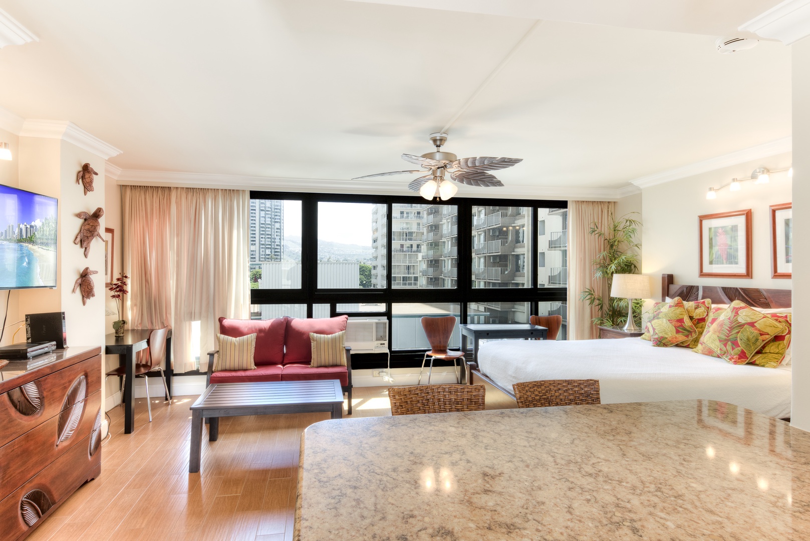 Relax in your bright, airy studio with tropical-inspired décor, comfy seating, and a ceiling fan. Large windows frame city views, while the cozy bed invites restful nights after exploring.