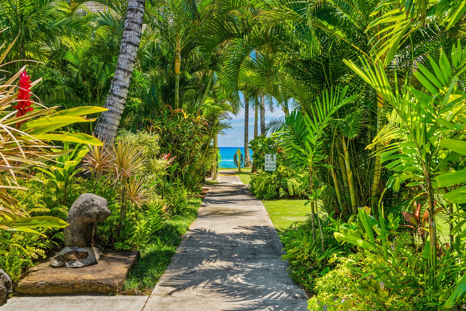 Tropical pathway through lush gardens leads to pristine beach access with turquoise waters beyond.