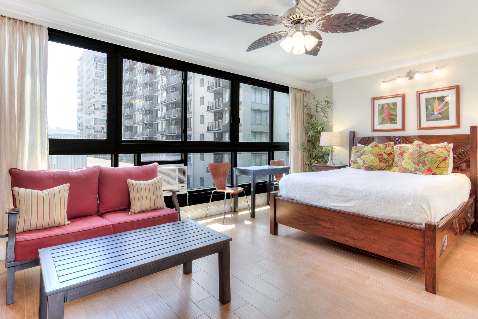 Your bright, tropical retreat features a king bed and lounge sofa with vibrant island-inspired decor, a ceiling fan keeping you cool, and stunning floor-to-ceiling windows framing city views.