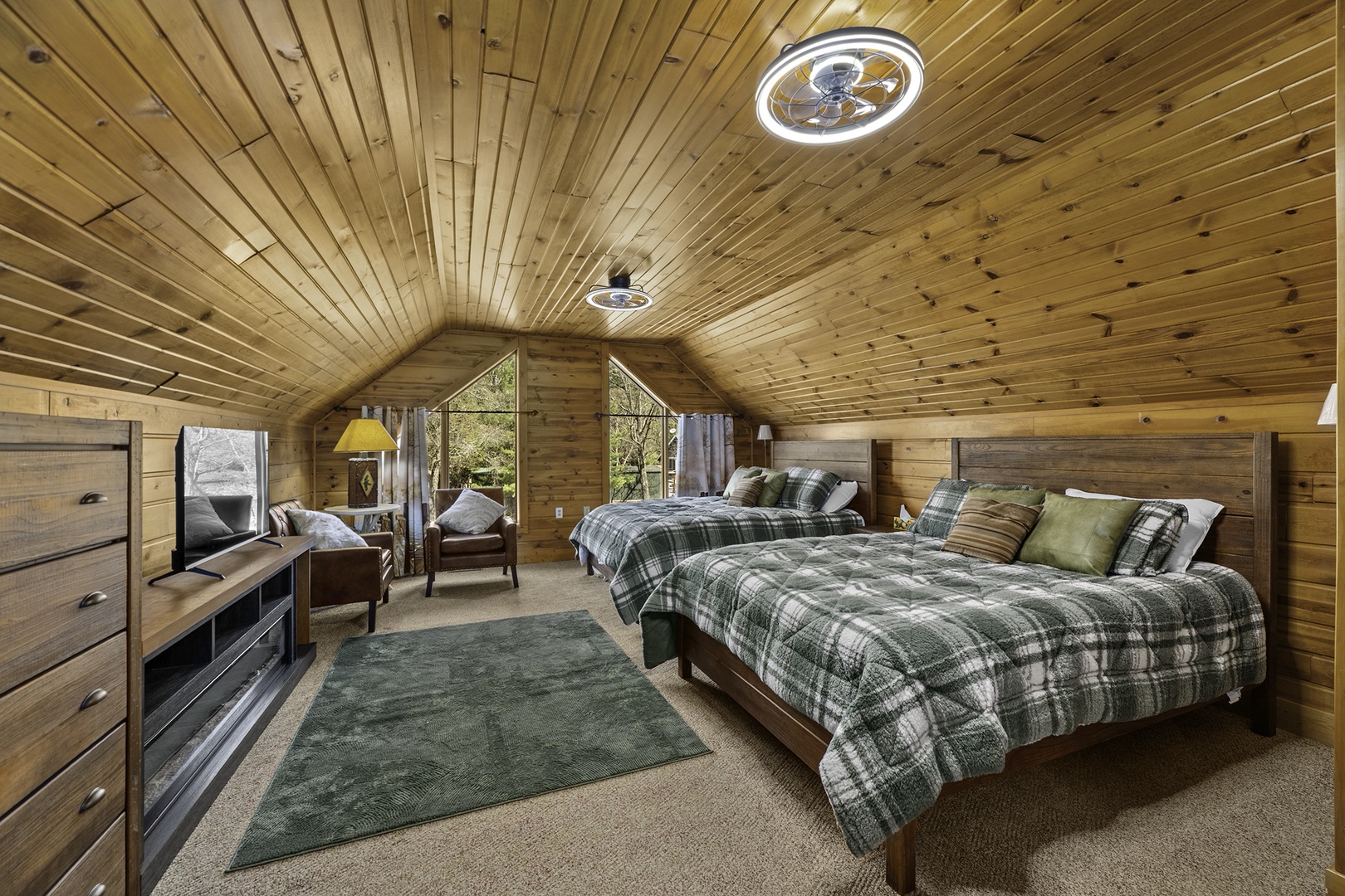 Cozy up in this charming wood-paneled bedroom featuring two plush beds with soft plaid bedding, vaulted ceilings, and peaceful forest views through large windows.