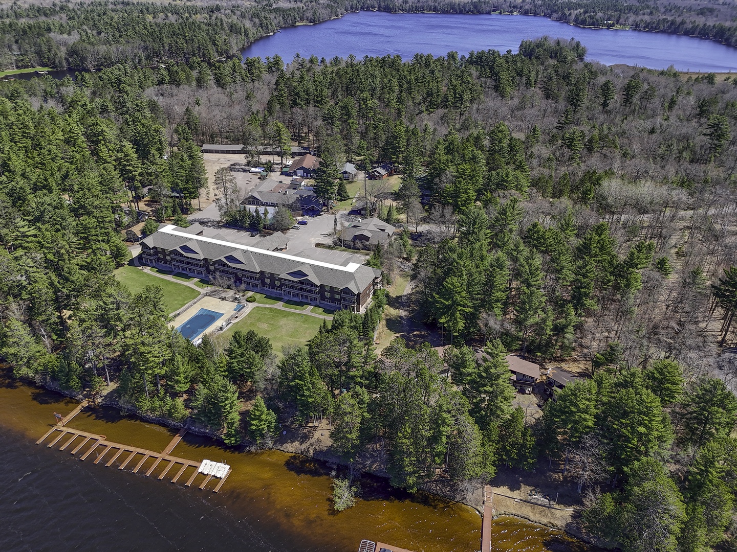 Aerial view of a lakefront resort property surrounded by dense forest and pristine waterways, offering a secluded natural setting with swimming pool and multiple recreational structures.