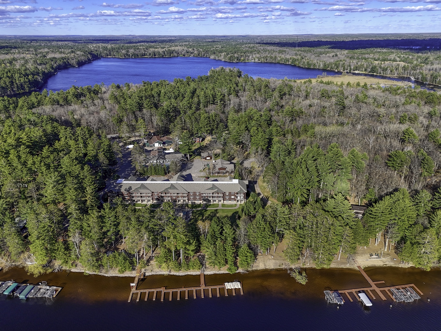 Aerial view of a lakefront resort property nestled among evergreen forests, featuring multiple buildings, private docks, and expansive natural surroundings across pristine lake waters.