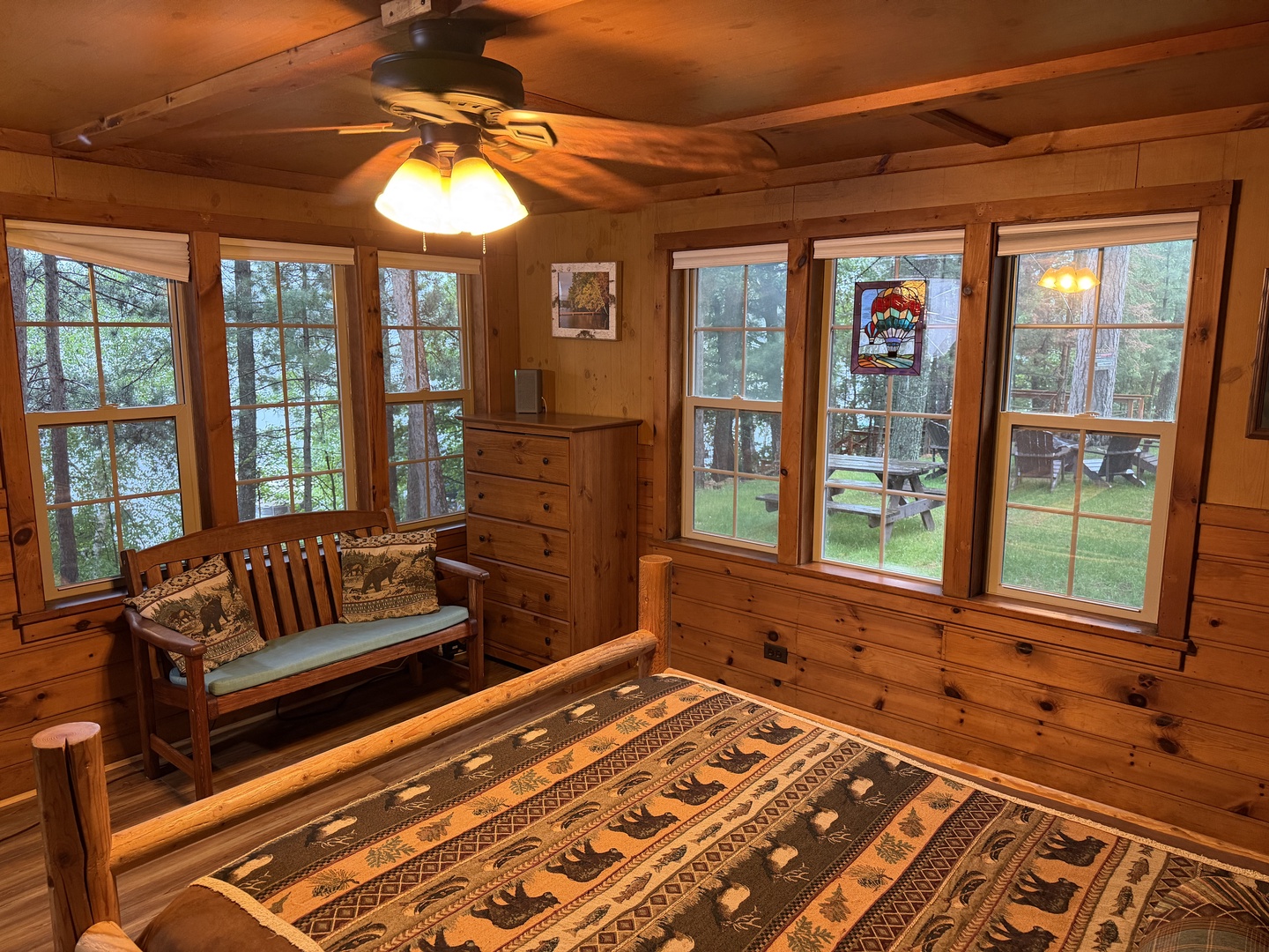 Unwind in your cozy pine-paneled bedroom where rustic charm meets comfort. Large windows frame peaceful forest views, while the ceiling fan keeps you cool and the warm wood creates your perfect mountain retreat.