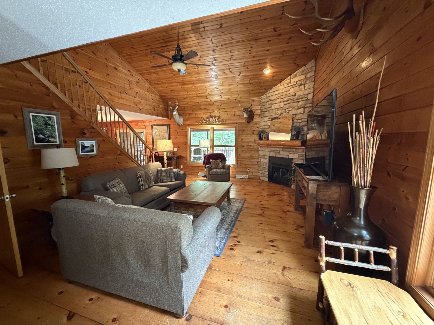 Settle into the warm embrace of this spacious cabin living room with soaring vaulted ceilings, rustic wood finishes, and a handsome stone fireplace where you can unwind after your adventures.