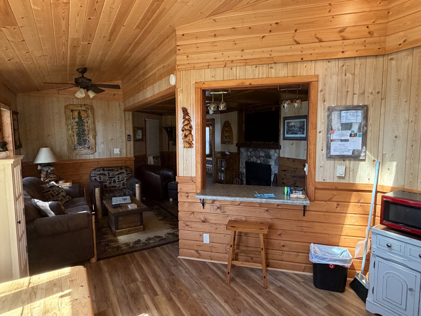 Step into your cozy cabin retreat with warm pine walls and vaulted ceilings. The open layout flows from living area to kitchen, featuring a breakfast bar and glimpse of the stone fireplace beyond.