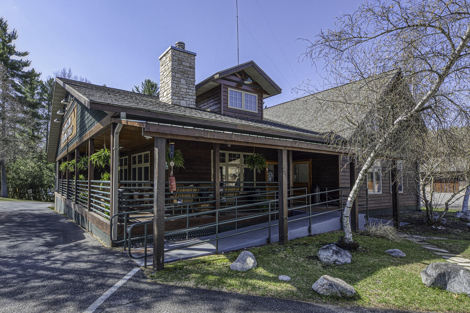 A charming  lodge featuring rustic wooden architecture and a welcoming covered porch, surrounded by natural beauty and mature trees in a peaceful wooded setting.