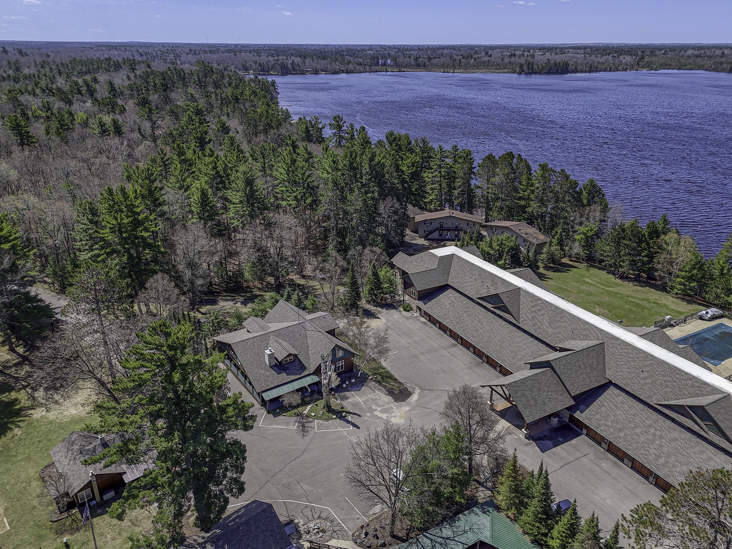 Aerial view of a secluded lakefront vacation property nestled among pine forests, featuring multiple buildings and  waterfront access on a peaceful Eagle lake.