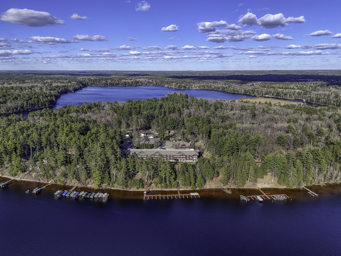 Aerial view of a lakeside vacation property nestled among forests, featuring boat docks and access to pristine waters surrounded by natural wilderness.