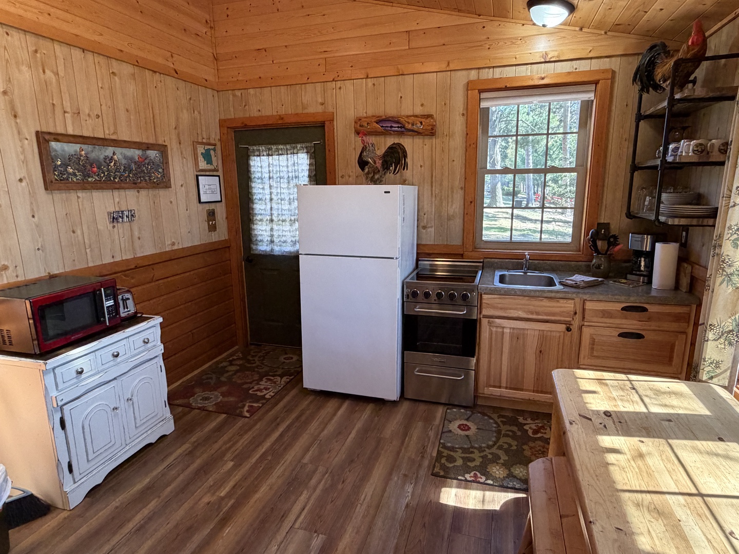 Step into your cozy cabin kitchen, where rustic charm meets convenience with full-size appliances, warm wood surroundings, and sunlight streaming through the windows—perfect for preparing home-cooked meals.