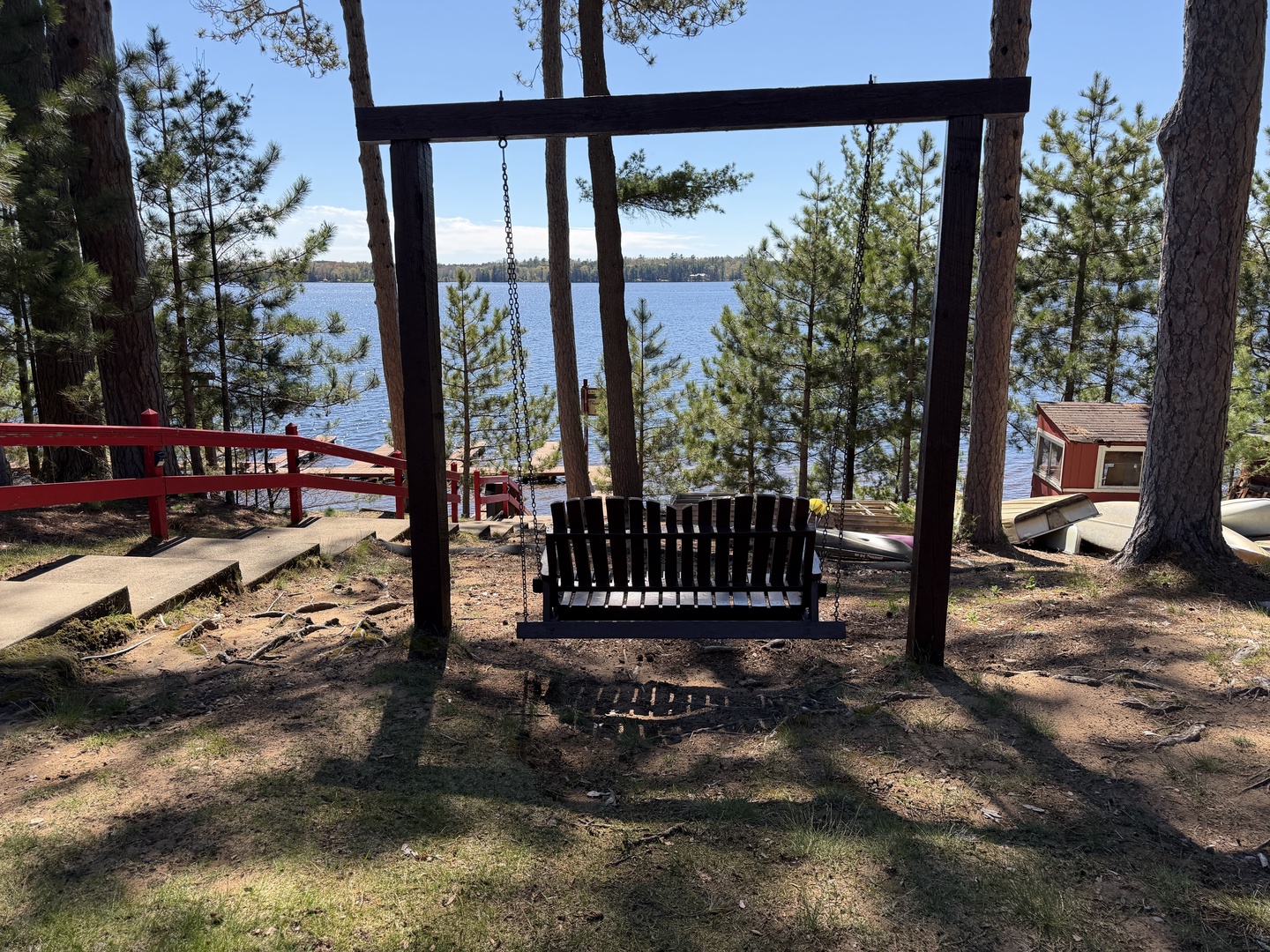 The property features a lakeside setting surrounded by towering pines. A wooden swing overlooks the water, offering a peaceful spot for relaxation amid natural scenery.