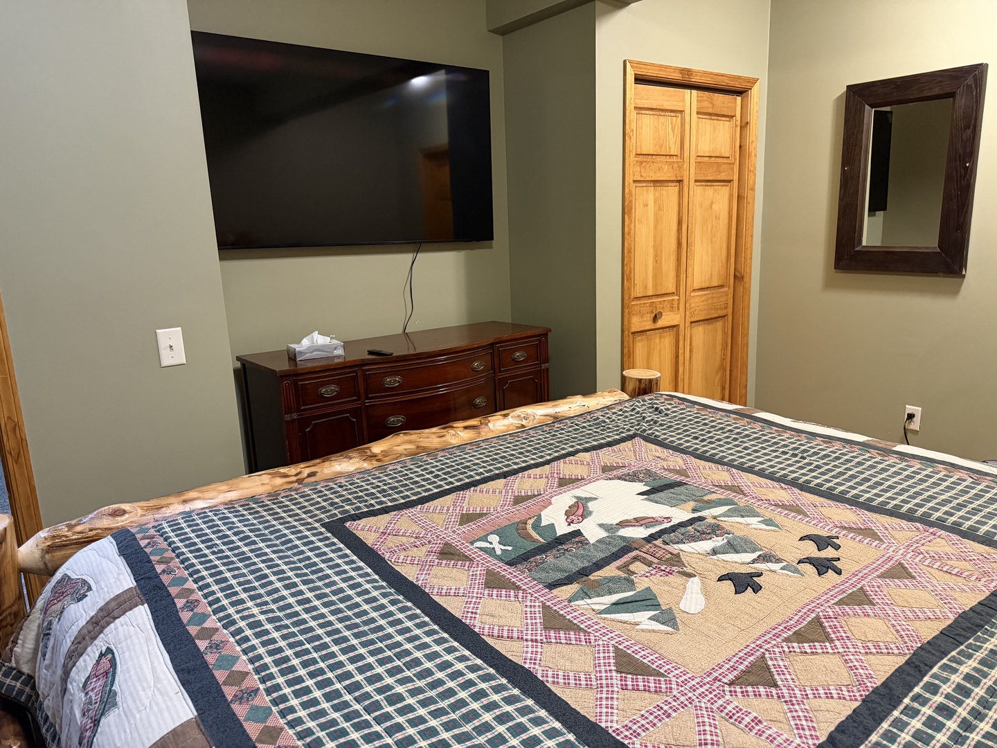 Relax in your inviting bedroom with a cozy quilt-covered bed, flat-screen TV, and rustic wooden wardrobe that adds charm and storage for your belongings.