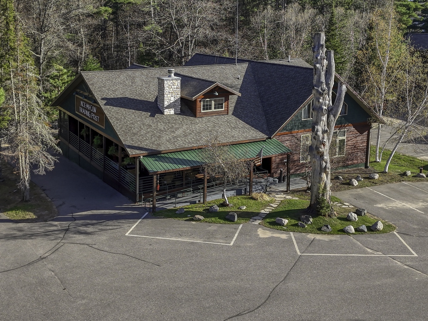 Aerial view of a rusticlodge with stone chimney, surrounded by forest. Ample parking and convenient access mark the arrival experience.