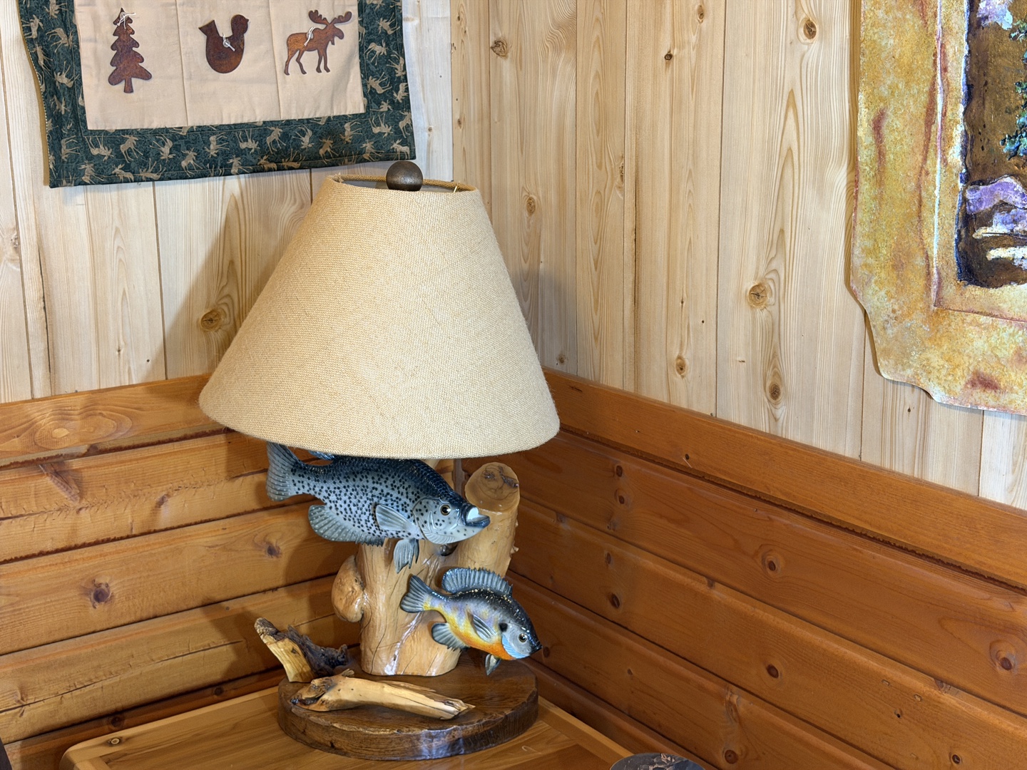 Charming cabin details greet you with warm wood tones and nature-inspired accents, from rustic quilts to a unique fish-themed lamp that sets a cozy, lakeside mood.