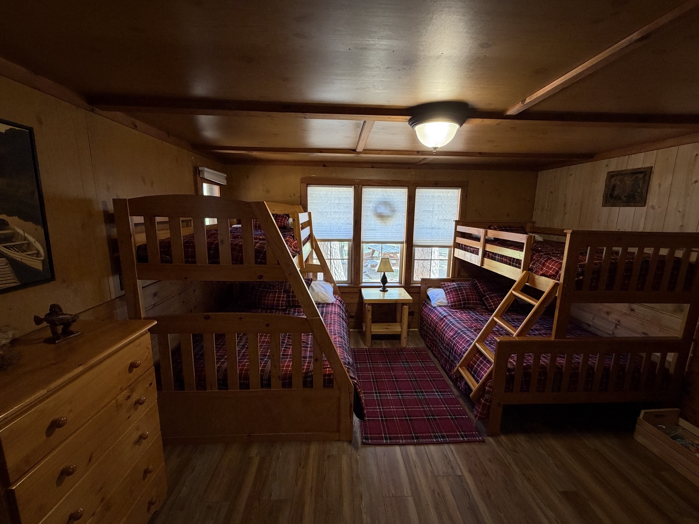 Your cozy cabin-style bedroom with rustic wood paneling and sturdy bunk beds draped in warm plaid linens invites the whole family to unwind together while daylight streams through lakeside windows.