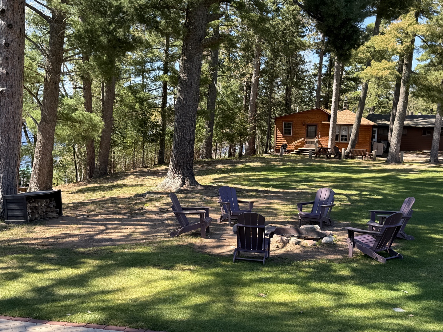 This property offers a tranquil wooded setting with a spacious lawn, a rustic cabin nestled among towering pines, and a cozy fire pit area perfect for evening gatherings.