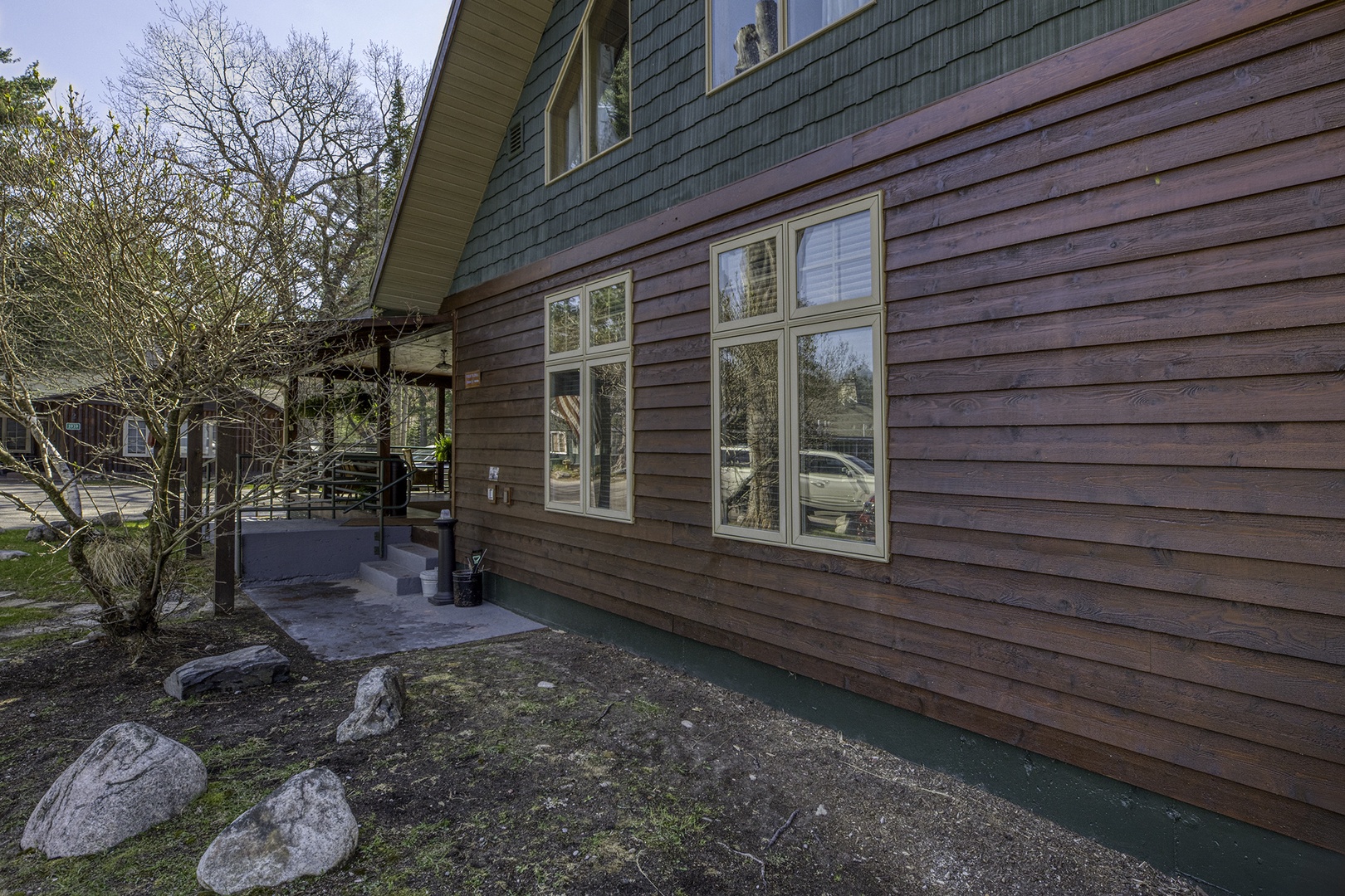 A welcoming two-tone cabin exterior with natural wood siding, large windows, and a peaceful front entrance surrounded by mature trees and landscaped grounds in a quiet resort