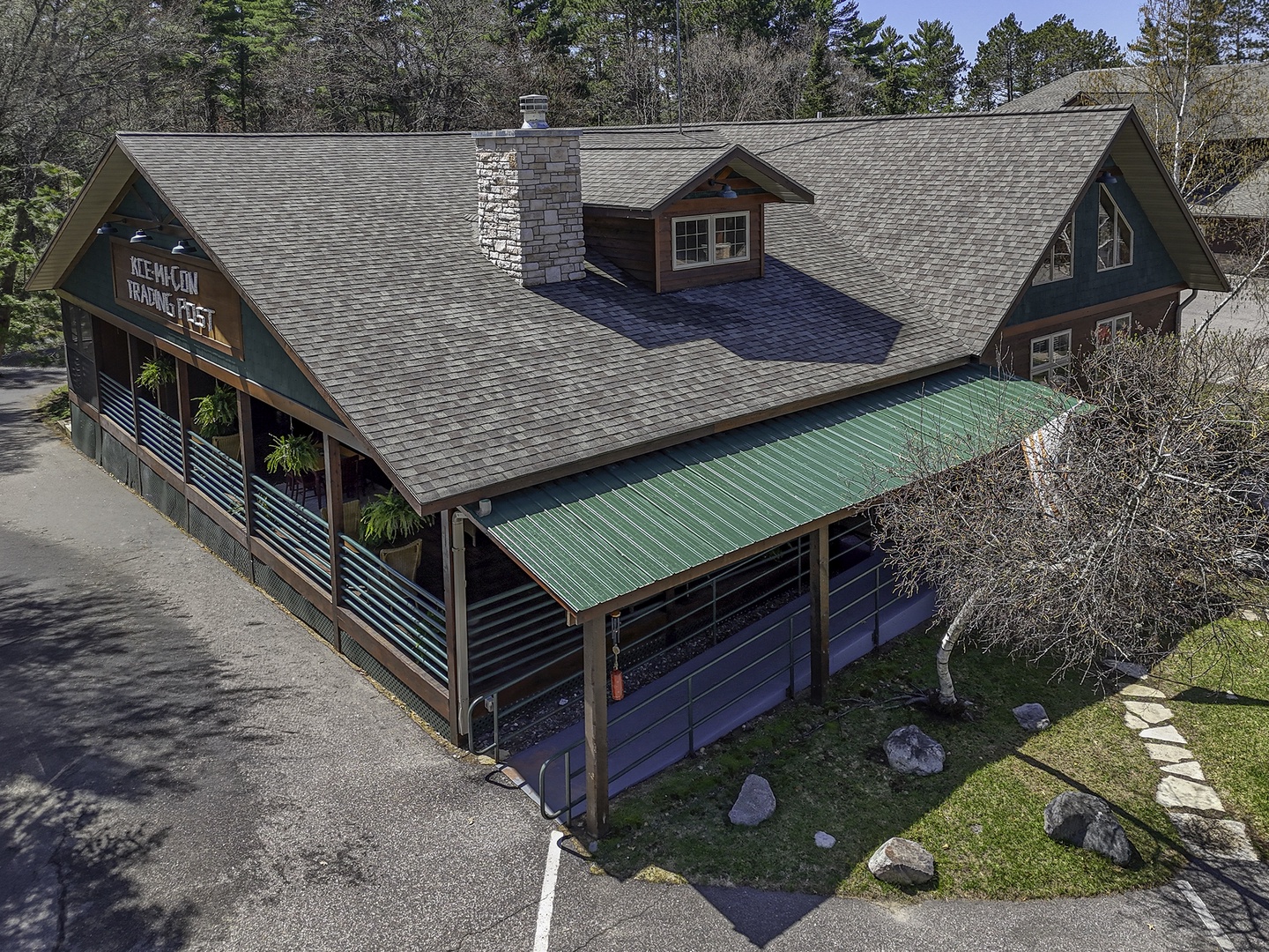 Aerial view of the property building showcasing its rustic architecture, stone chimney, covered porch area, and natural wooded surroundings.