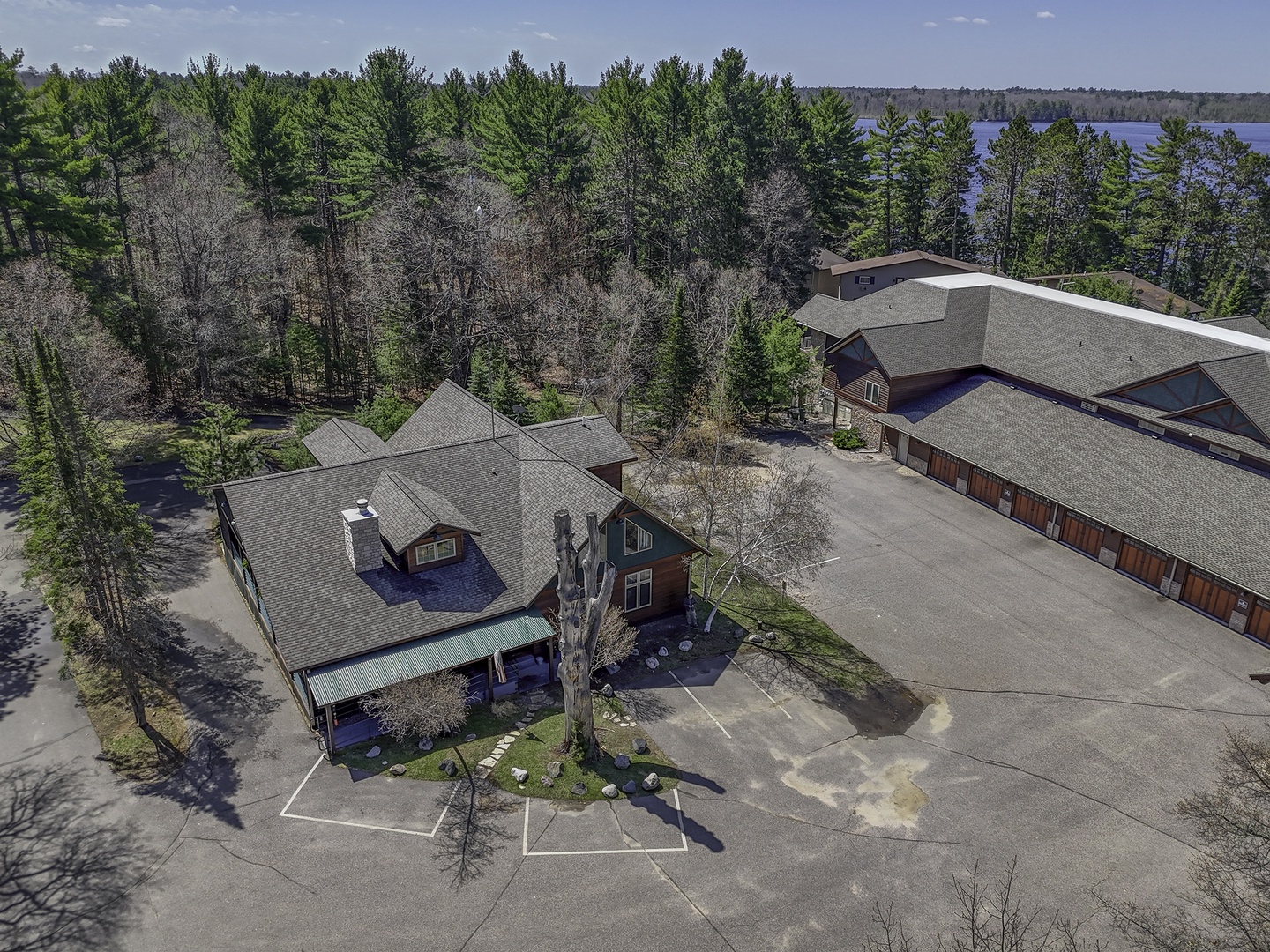 Aerial view of the property nestled among mature pines with a scenic lake visible through the trees beyond.