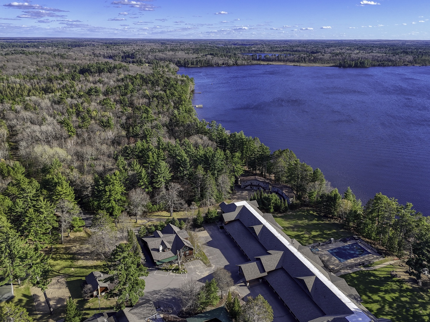 Aerial view showcasing a peaceful lakefront retreat surrounded by dense forest, offering a secluded escape with direct water access and expansive natural scenery.