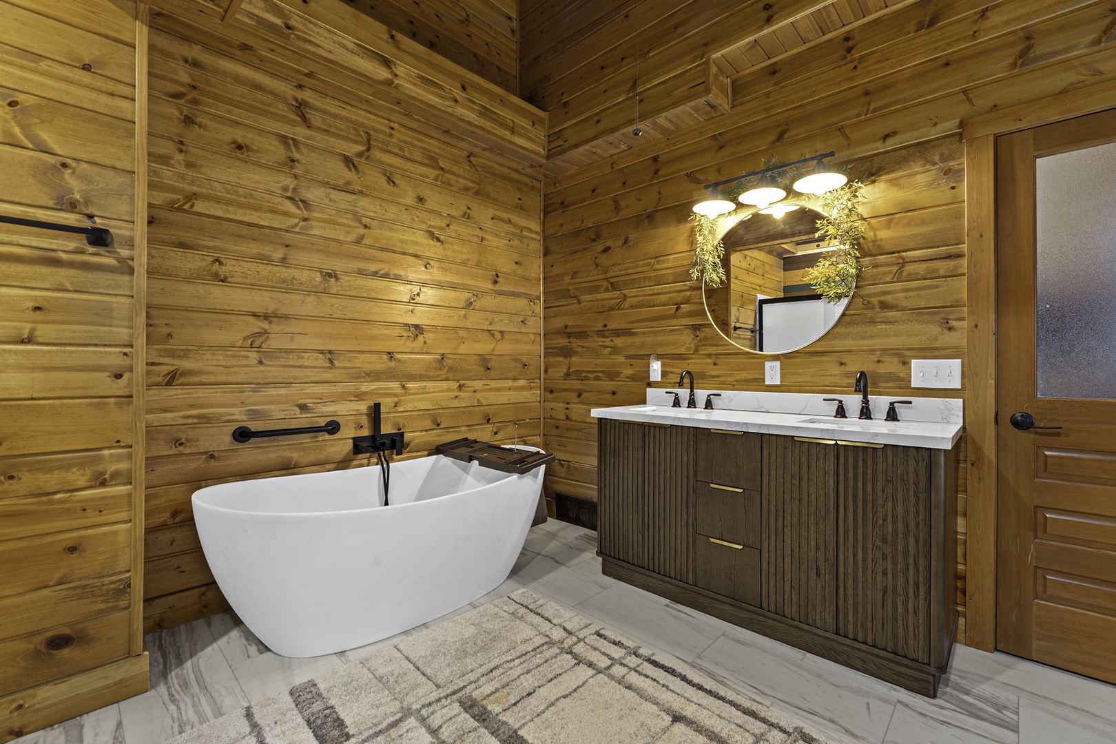 Sink into the freestanding soaking tub surrounded by warm wood walls, where dual vanities and modern fixtures blend rustic charm with spa-like comfort.